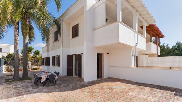 A two-story building with a balcony, a tiled patio, and palm trees. - 2811 Villetta Altomare by Barbarhouse (Porto Cesareo)