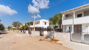 A residential street with white houses, a paved road, and a clear blue sky. - 2811 Villetta Altomare by Barbarhouse (Porto Cesareo)