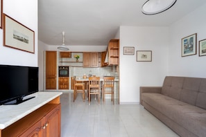Une cuisine moderne avec des meubles en bois, une table à manger et des chaises. On y trouve également un téléviseur à écran plat posé sur un meuble, un canapé et des tableaux encadrés accrochés au mur.