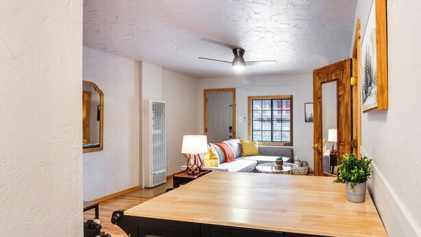 A kitchen with a wooden countertop, a ceiling fan, a window with a view, and a sofa in the background.