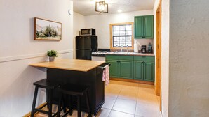 A compact kitchen with a wooden island, green cabinets, and a small window.