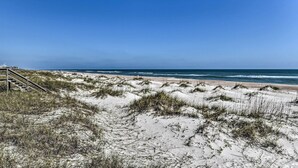 Ein Strand mit Sanddünen und einer Holztreppe, die zum Strand hinabführt.