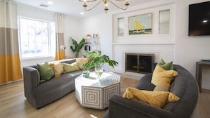 A living room with two grey sofas, a coffee table, a fireplace, and a large window with curtains.