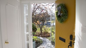 A doorway leading to a garden with a yellow wall, a wreath, and a small tree.
