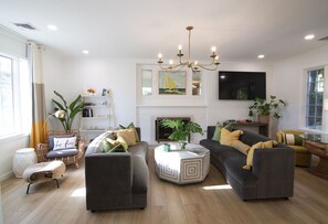 Un salon moderne avec une cheminée, un lustre et un téléviseur à écran plat.