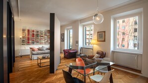 A spacious living room with a wooden floor, a glass coffee table, and a sofa. There is a bookshelf filled with books and a window with a view of buildings. - Wonderful 1 Bedroom Apartament in the City Center (Rome)