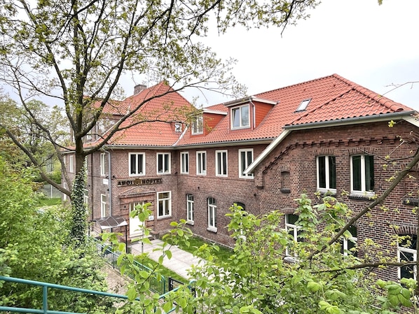 A two-story brick building with a red-tiled roof, multiple windows, and a visible staircase leading to the upper floor.