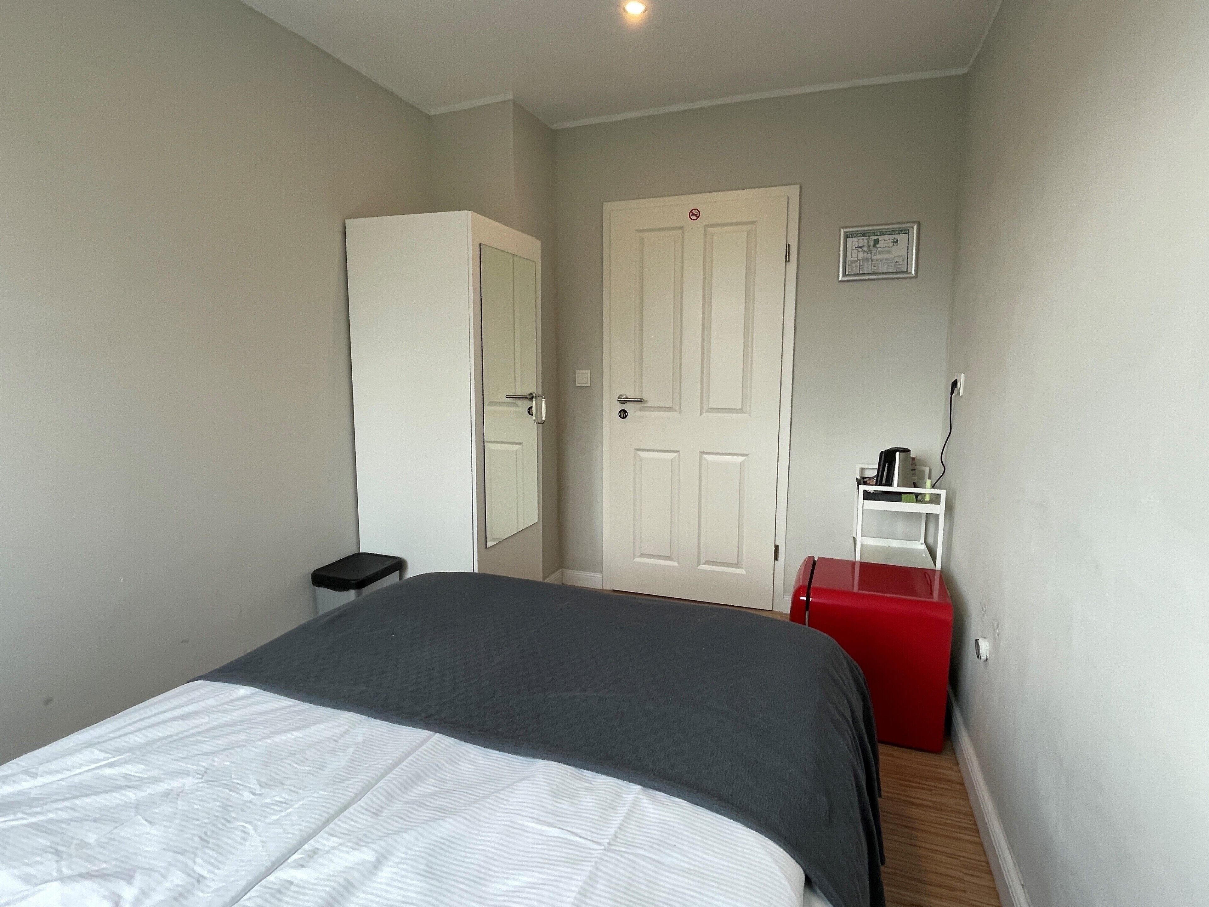 A bedroom with a bed, a wardrobe, a door, and a small table with a red box.