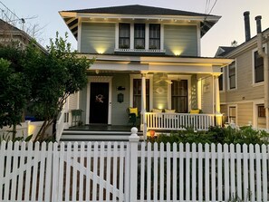 Una casa a due piani con veranda, recinzione di steccati bianchi e porta d'ingresso decorata con un'ghirlanda di fiori.