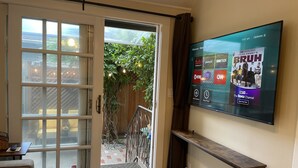 Un salón con una puerta corrediza de cristal que da a un balcón, un televisor de pantalla plana montado en la pared y un banco de madera.