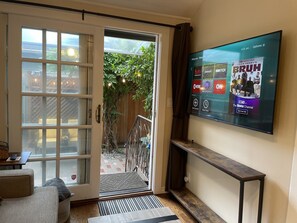 Un soggiorno con una porta-finestra che si apre su un balcone, una TV a schermo piatto montata a parete e una panca in legno.