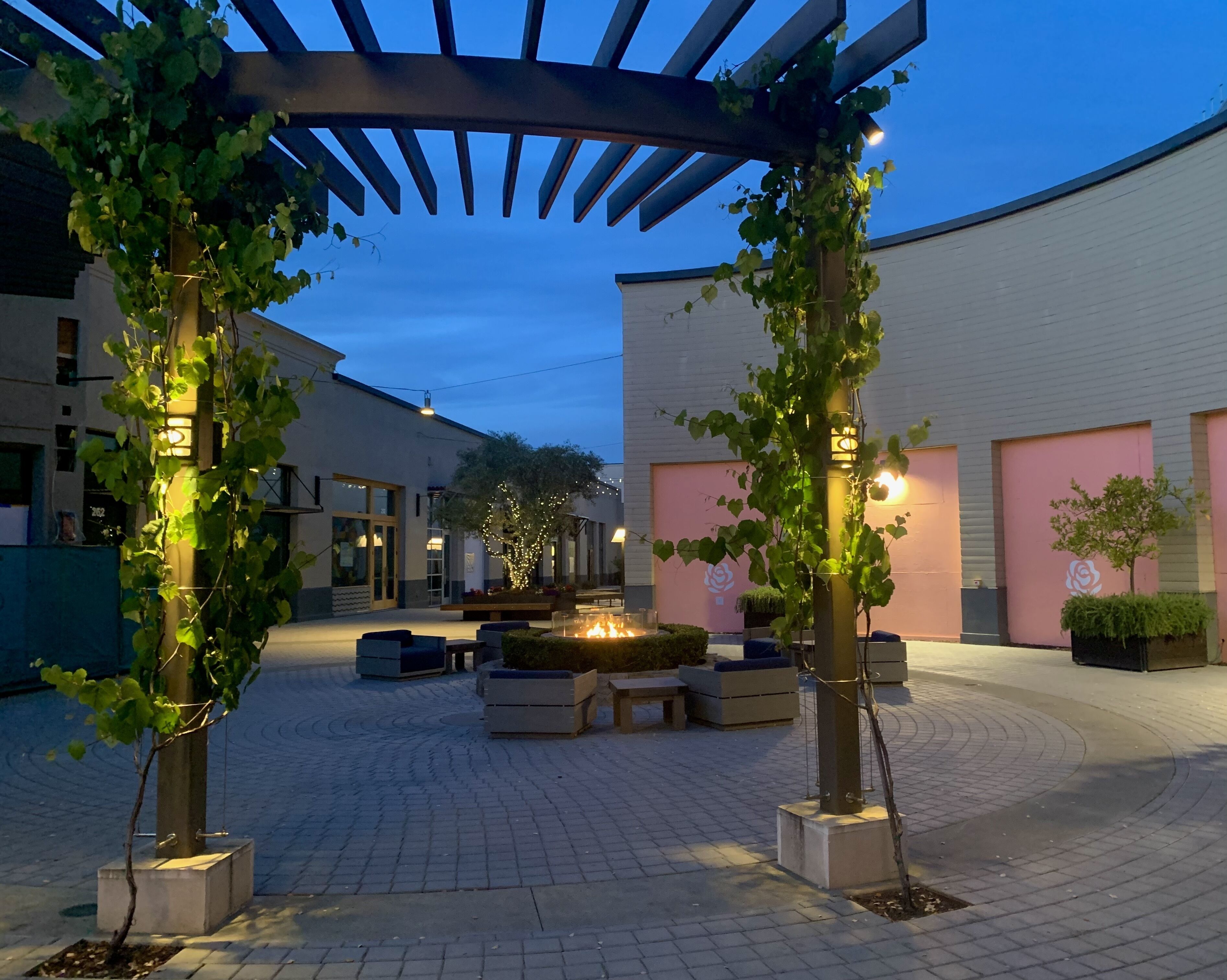 An outdoor courtyard with a pergola, seating areas, and a fire feature.