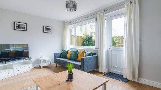 A modern living room with a grey sofa, a wooden coffee table, a TV, and a large window with curtains. - Howick House-sleeps 5-pet Friendly-parking-garden (Newcastle-upon-Tyne)