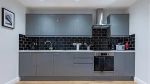 A modern kitchen with grey cabinets, a stainless steel range hood, a built-in oven, and a black tiled backsplash. - Howick House-sleeps 5-pet Friendly-parking-garden (Newcastle-upon-Tyne)