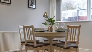 A dining table set for four with white chairs and a plant centerpiece. - Howick House-sleeps 5-pet Friendly-parking-garden (Newcastle-upon-Tyne)