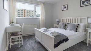 A bedroom with a bed, bedside tables, a chair, a window with curtains, and framed pictures on the wall. - Howick House-sleeps 5-pet Friendly-parking-garden (Newcastle-upon-Tyne)