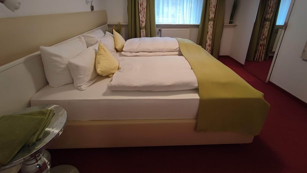 A hotel room with a bed, pillows, a bedside table, and a window with curtains. - Room in Guest Room - Pension Forelle - Doppelzimmer (Forbach)