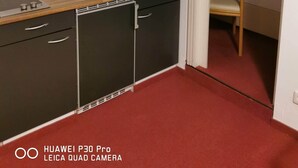 A compact kitchen with a sink, a small dishwasher, and dark cabinets. A wooden countertop and a red carpeted floor are also visible. - Room in Guest Room - Pension Forelle - Doppelzimmer (Forbach)