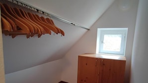 A small, sloped room with a wooden wardrobe, a coat rack with hangers, and a window providing natural light. - Room in Guest Room - Pension Forelle - Doppelzimmer (Forbach)