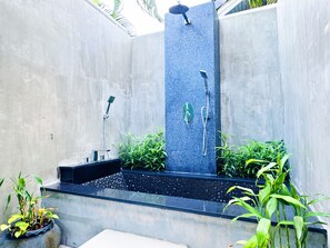 A modern outdoor shower area with a vertical water feature, a seating bench, and potted plants.