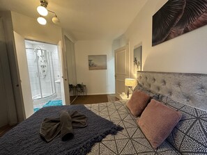 Quarto com cama, cabeceira, mesa de cabeceira, luminária e área de chuveiro.