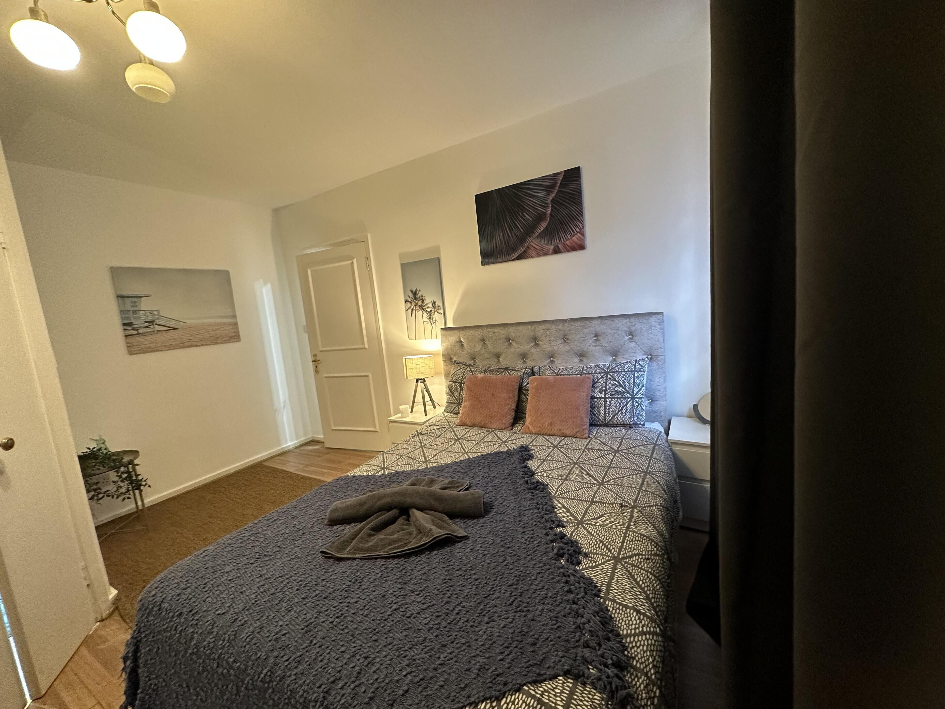 A bedroom with a bed, a bedside lamp, a wall-mounted artwork, and a door.