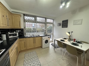 Cozinha compacta com máquina de lavar, área de refeições com mesa posta para dois e janela com vista para edifícios.