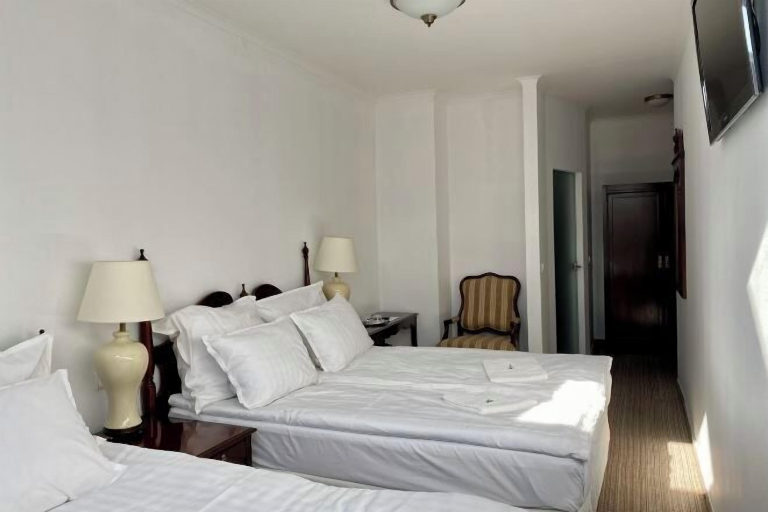 A hotel room with two beds, a chair, a desk, and a television.