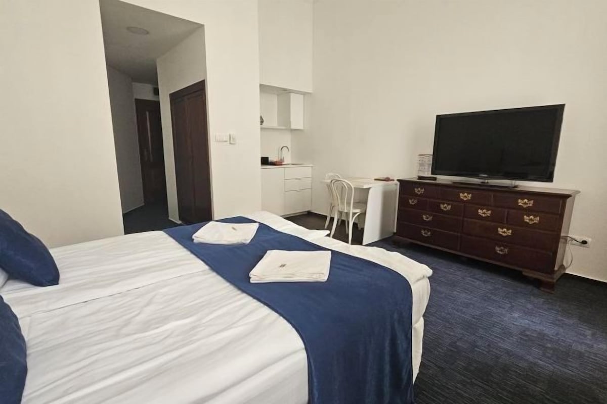 A hotel room with a bed, a TV, a dresser, and a desk with a chair.