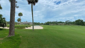 Un campo de golf con un club de campo, búnkeres de arena y un amplio lago.