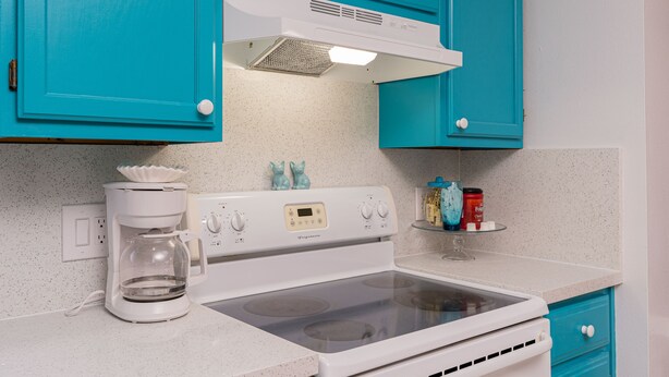 Een keuken met turquoise kastjes, een witte kookplaat en een koffiezetapparaat.