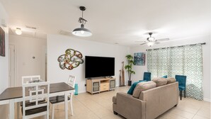 Een woonkamer met een televisie, bank, stoelen en een eettafel.