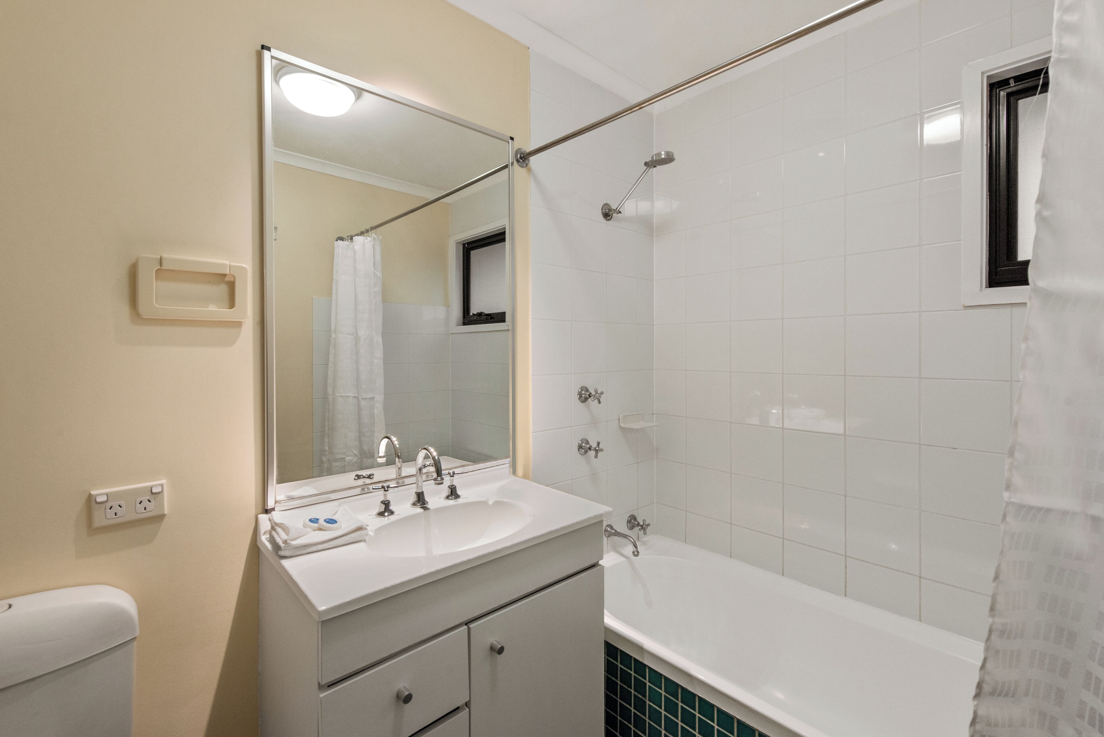 A bathroom with a white sink, mirror, and bathtub. There is a showerhead above the bathtub and a towel rack on the wall.
