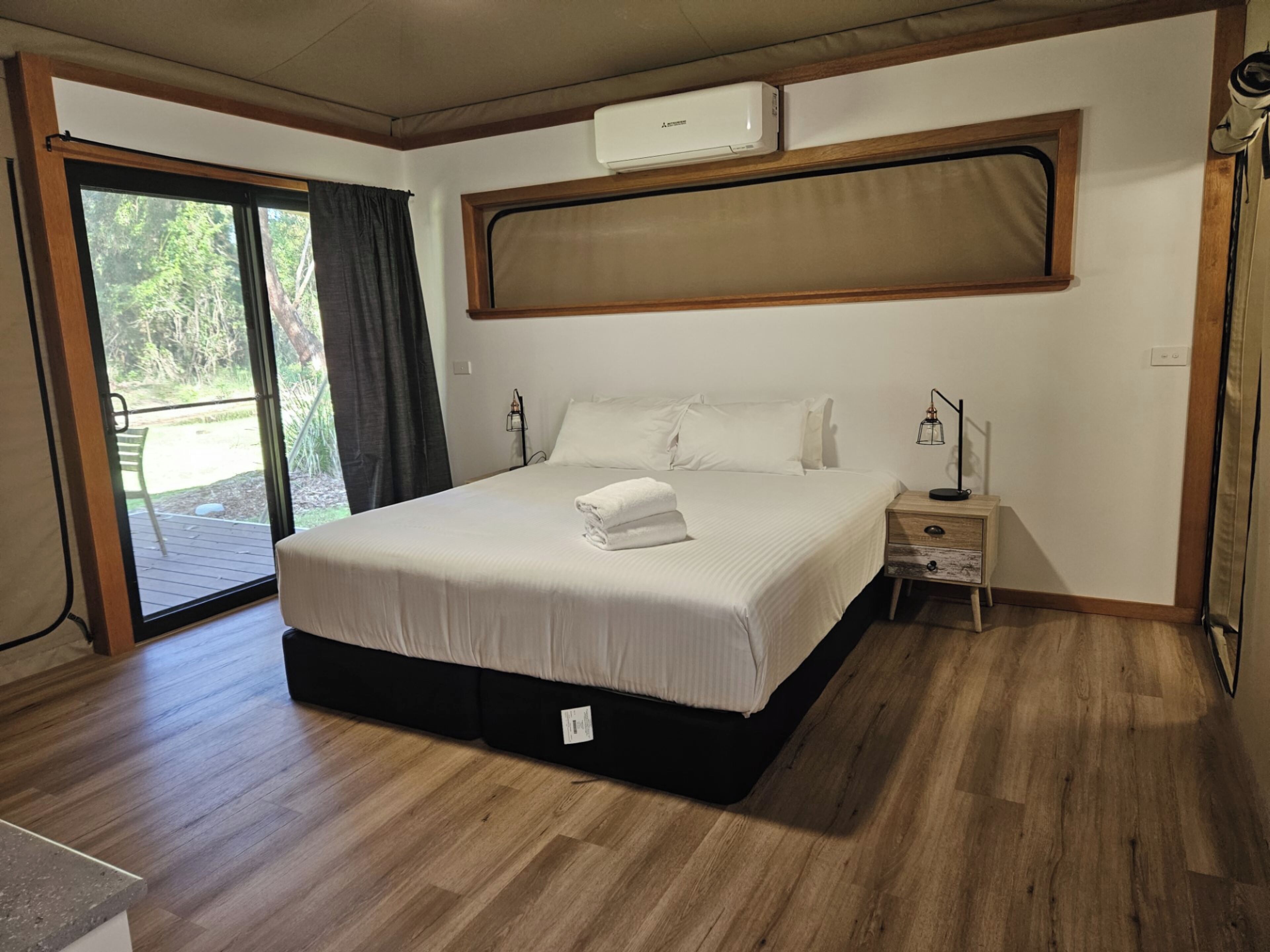 Un dormitorio con cama, mesita de noche, equipo de aire acondicionado y puerta corrediza de vidrio a un patio.