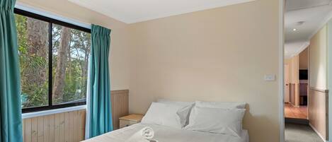 Habitación de hotel con cama, mesita de noche, ventana con cortinas y vistas a árboles.