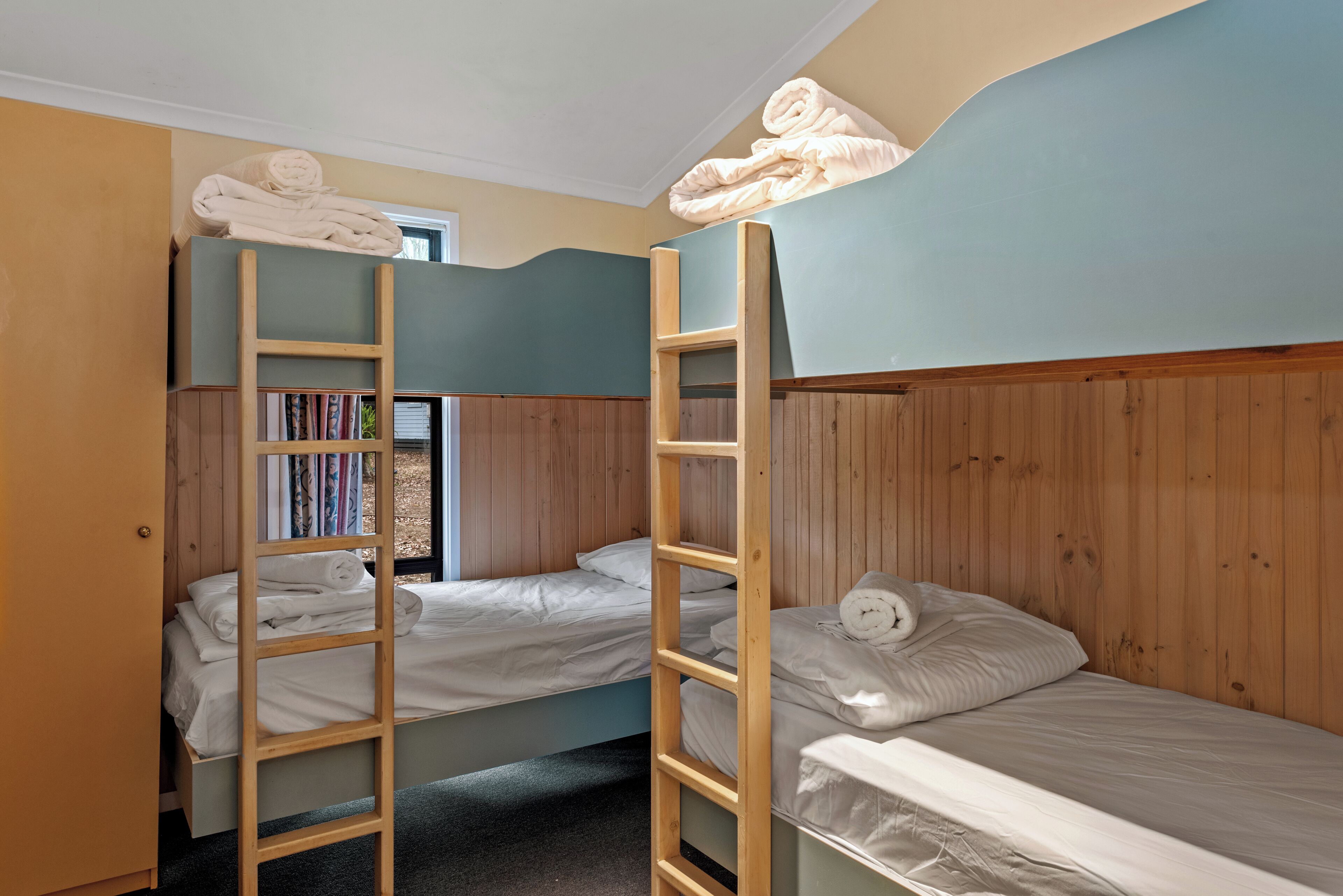 A dormitory room with bunk beds, wooden ladders, and a bookshelf.