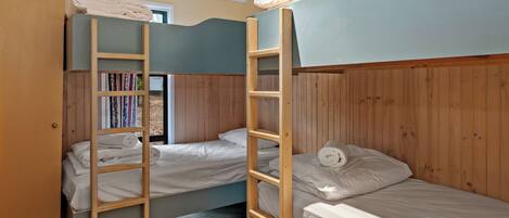 A dormitory room with bunk beds, wooden ladders, and a bookshelf.