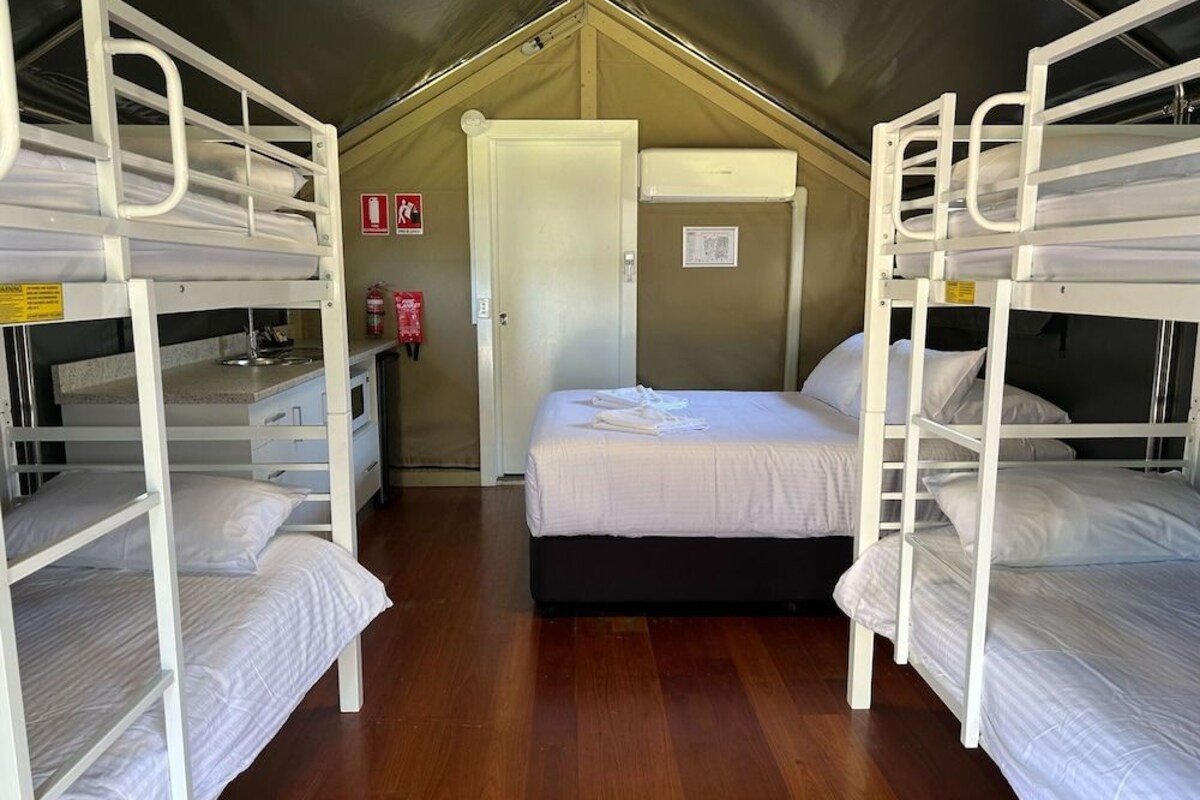 A dormitory-style room with bunk beds, a small desk, and a door leading to another room.