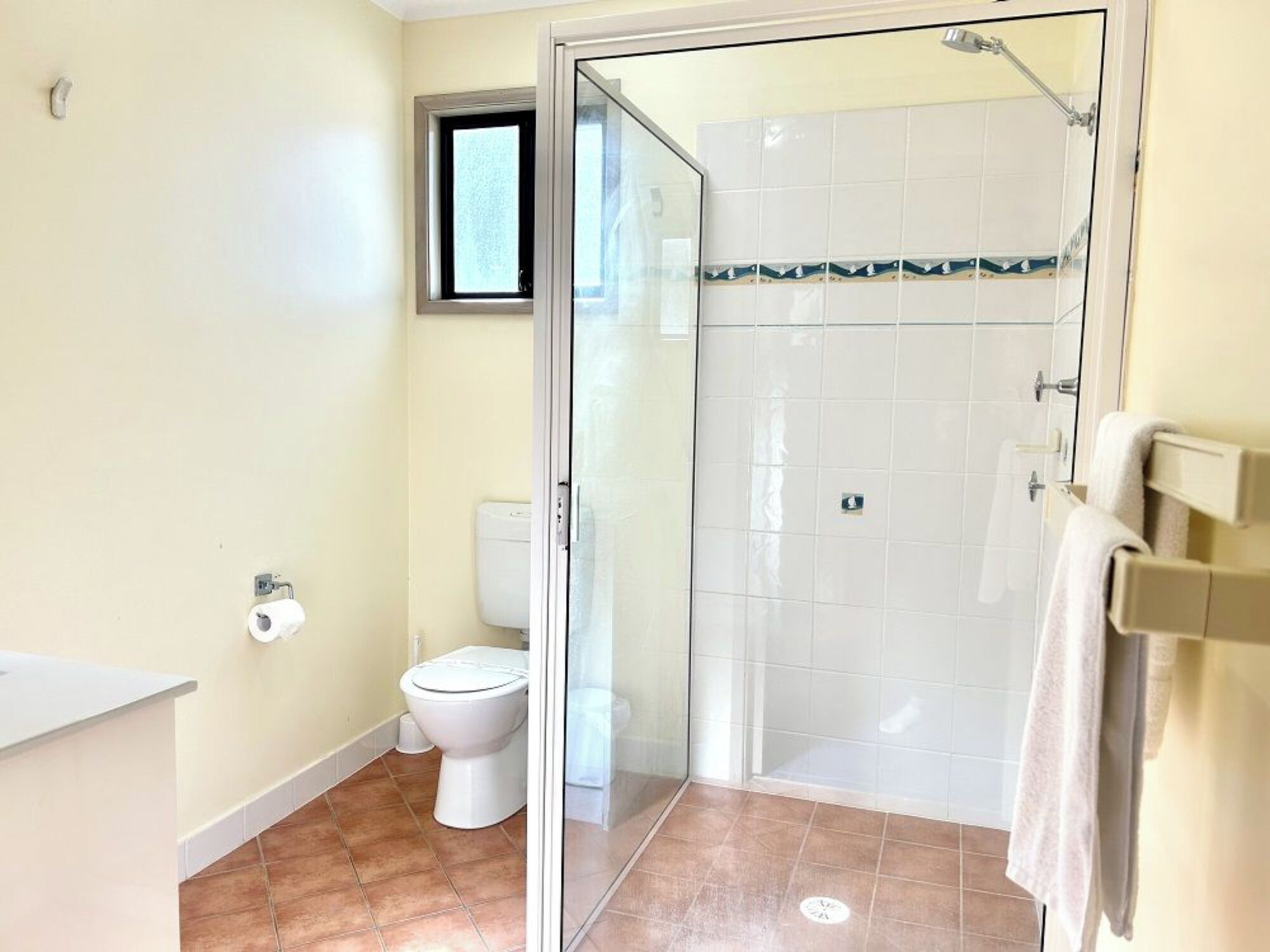 A bathroom with a toilet, a shower with a glass door, and a window.