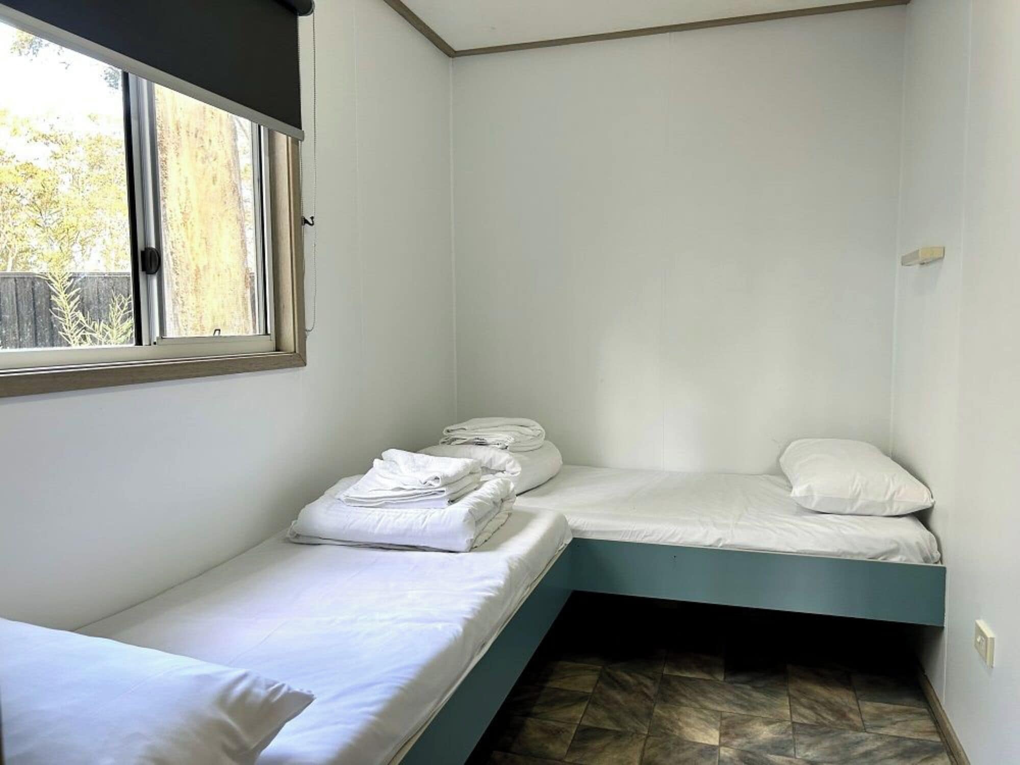 A small, single-room accommodation with a window, a bed, and a bench.