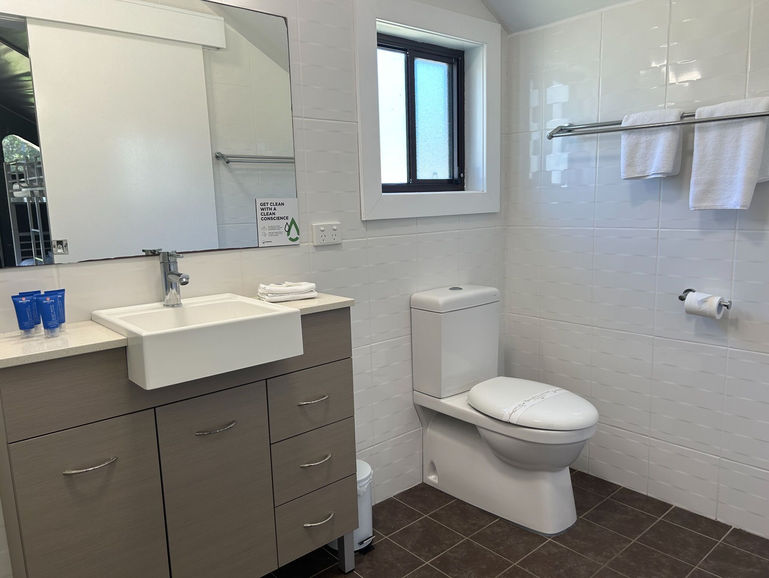 Un baño moderno con lavamanos, espejo, inodoro y ventana.