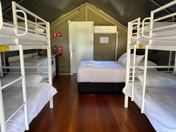 A dormitory room with bunk beds, a kitchenette, a fire extinguisher, and a door leading to another room.