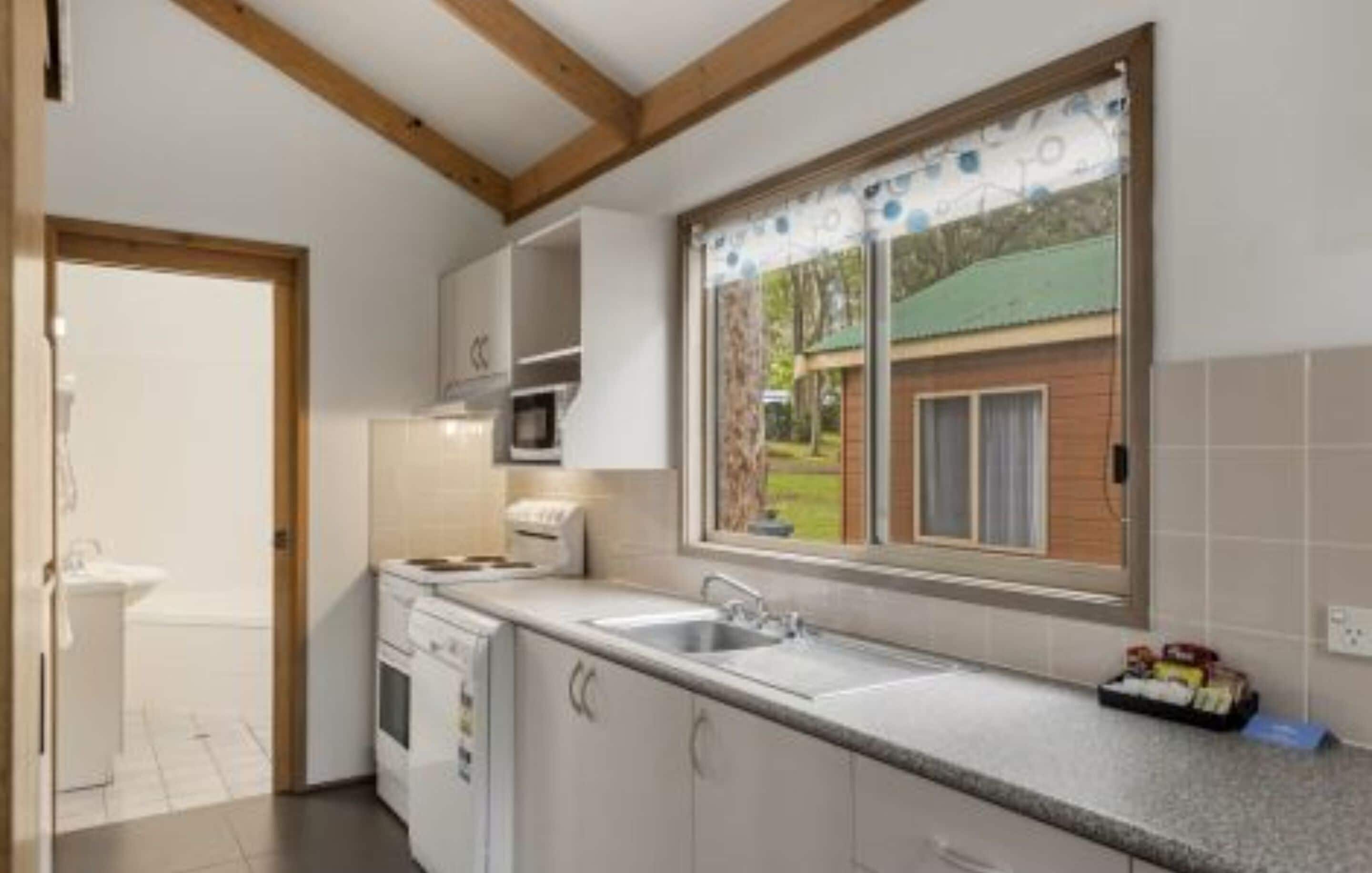 A kitchen with a window, white cabinets, a microwave, and a sink.