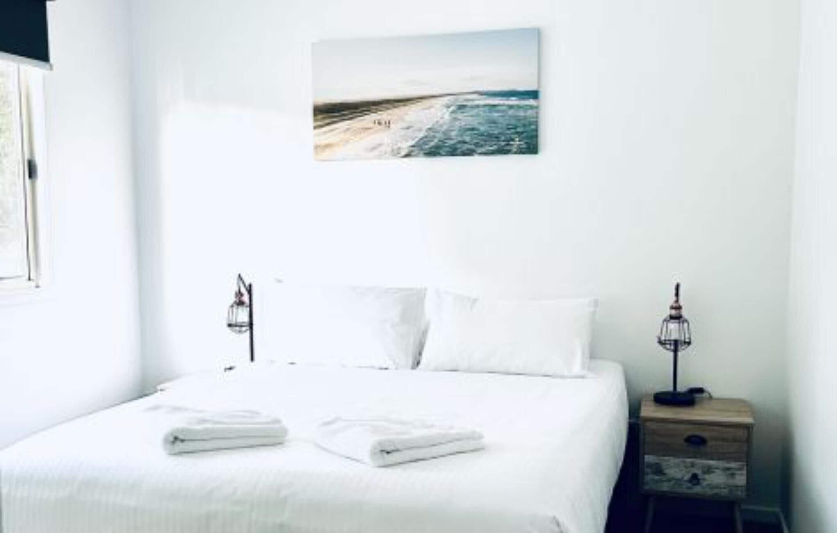 A neatly made bed with white linens and two bedside lamps on a wooden nightstand.