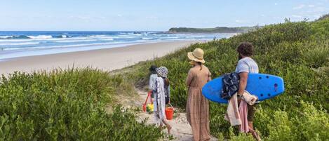A beach path with greenery, a sandy beach, and the ocean.