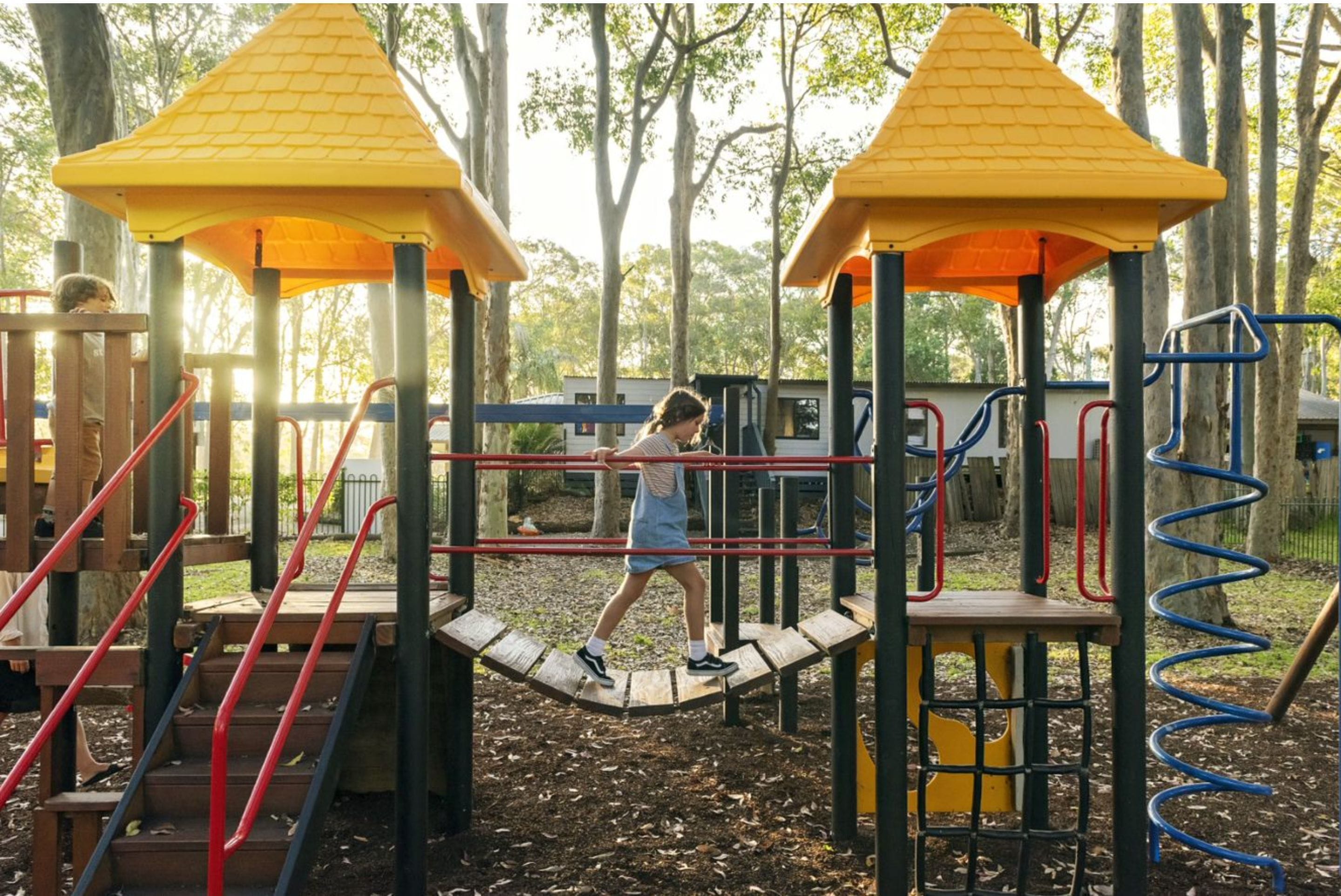 A playground with a wooden climbing structure, a slide, and a swing set.