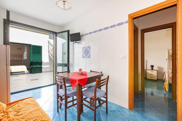 A dining area with a table set for four, a television mounted on the wall, and a balcony door leading outside.