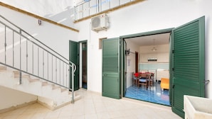 Um edifício residencial com escadaria, portas verdes abertas que dão acesso a uma sala de jantar e chão de azulejos.