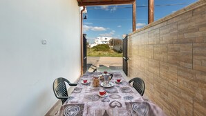 Un pequeño patio al aire libre con una mesa preparada para dos personas, con mantel estampado, cafetera, tazas y un tarro de galletas.