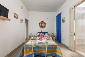 Uma área de refeições com uma mesa posta para quatro pessoas, uma TV na parede e um painel decorativo em forma de sol.